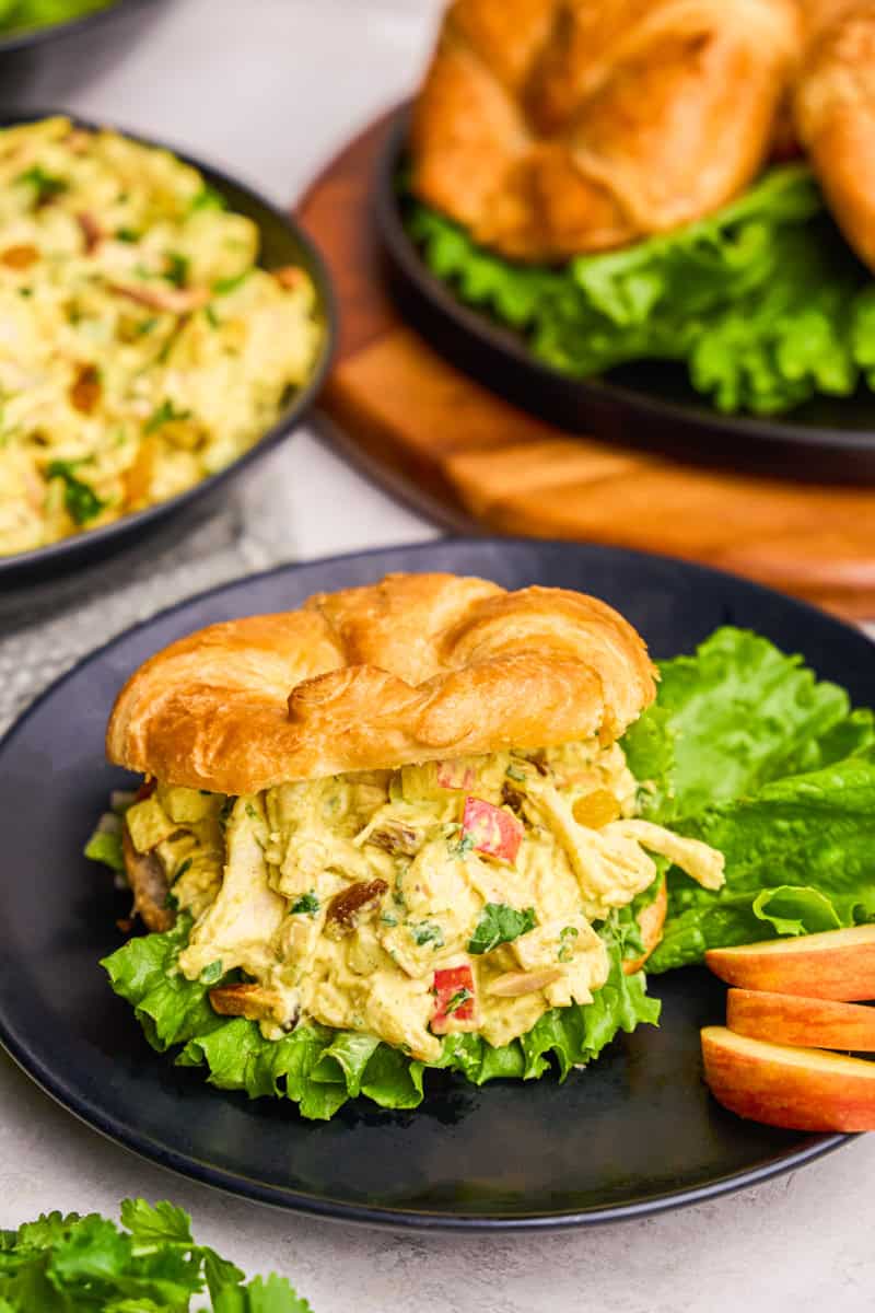 Curry Chicken Salad in a croissant on a plate with apples and lettuce.