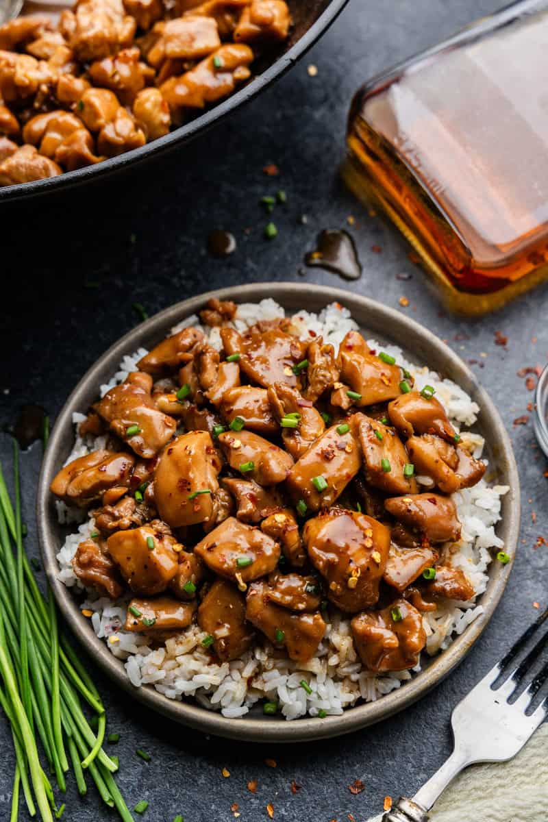Overhead shot or bourbon chicken on a plate of rice with bourbon in background.
