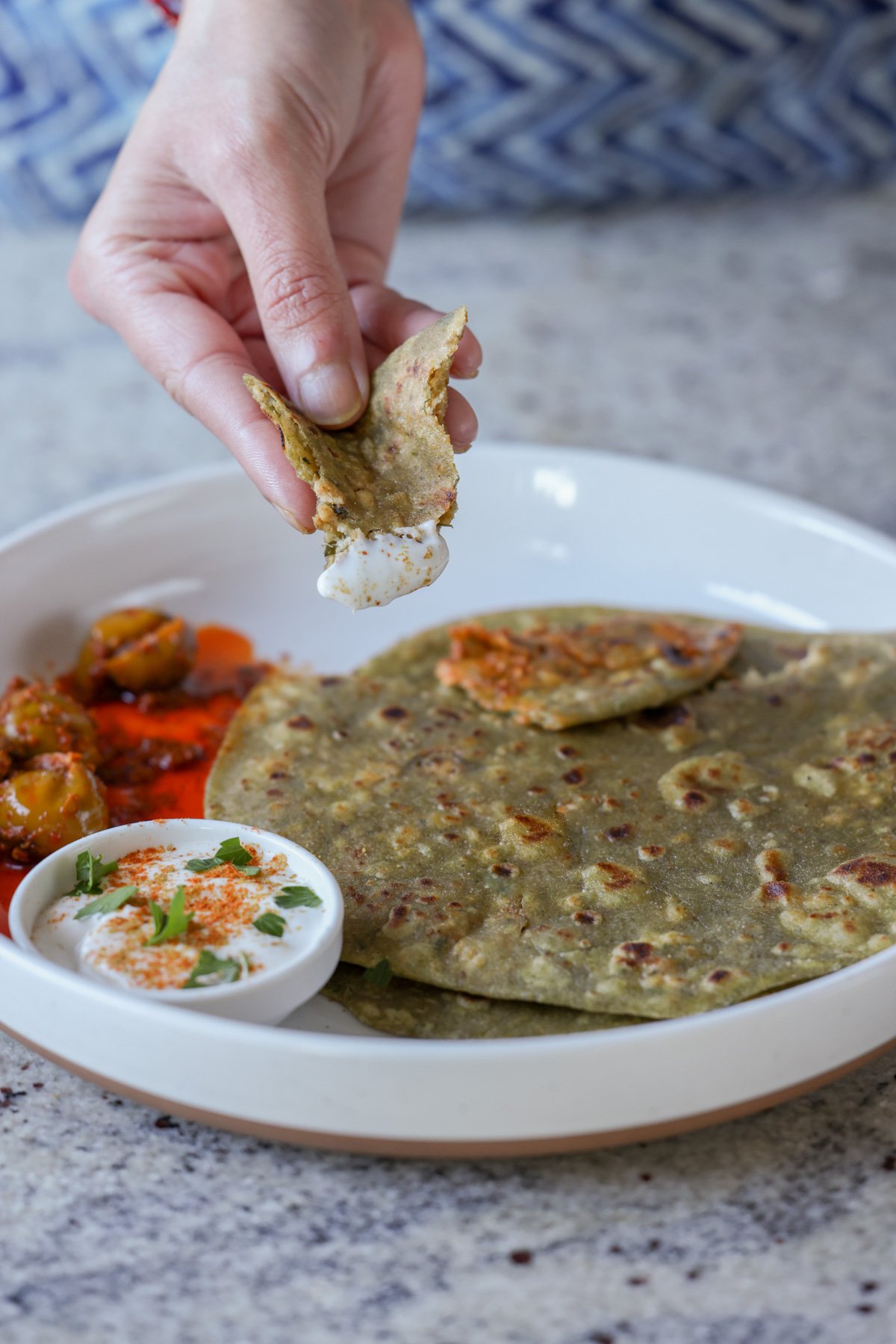 hand dipping a piece of spinach paratha into raita