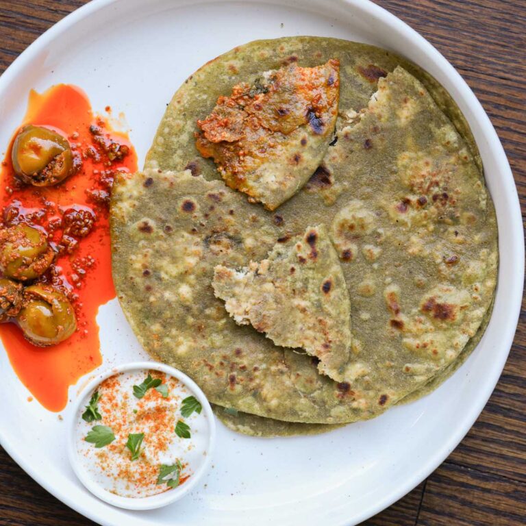 spinach paratha on a plate with raita and Indian pickle