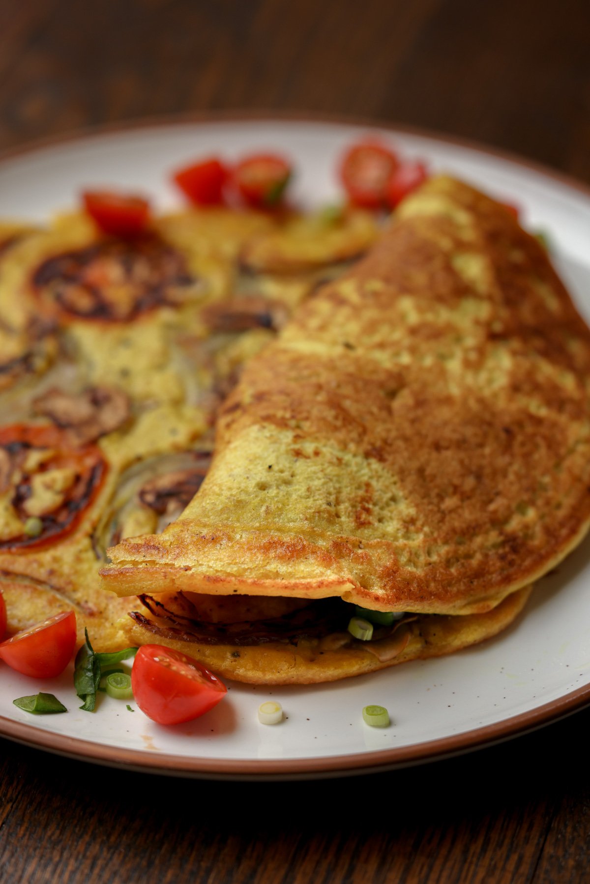 chickpea omelette with veggies inside next to one prepared with the fillings stuffed into the folded omelet