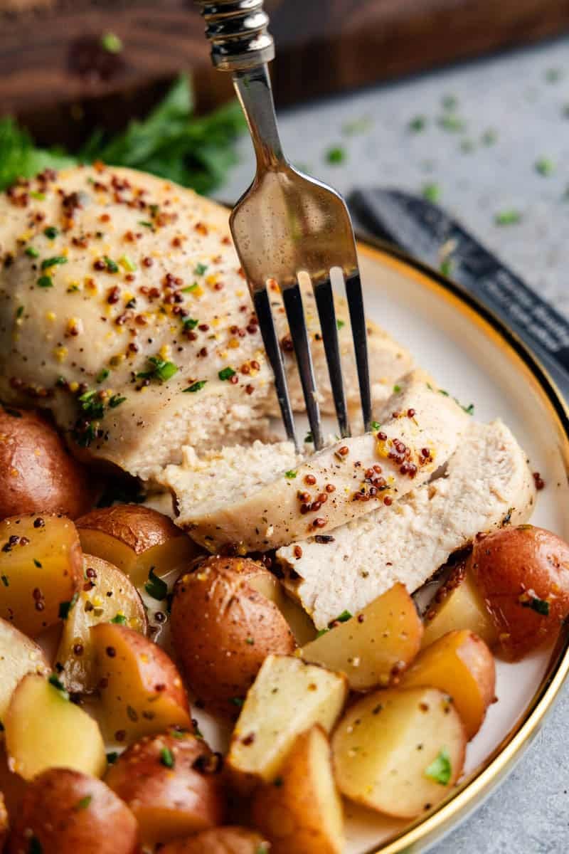 Fork bite of baked honey dijon chicken and potatoes on a plage with mini potatoes.