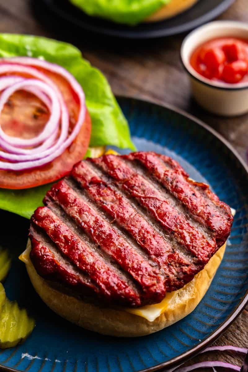 A smoked burger patty sitting atop a bun on a plate ready to be sandwiched into a smoked burger.