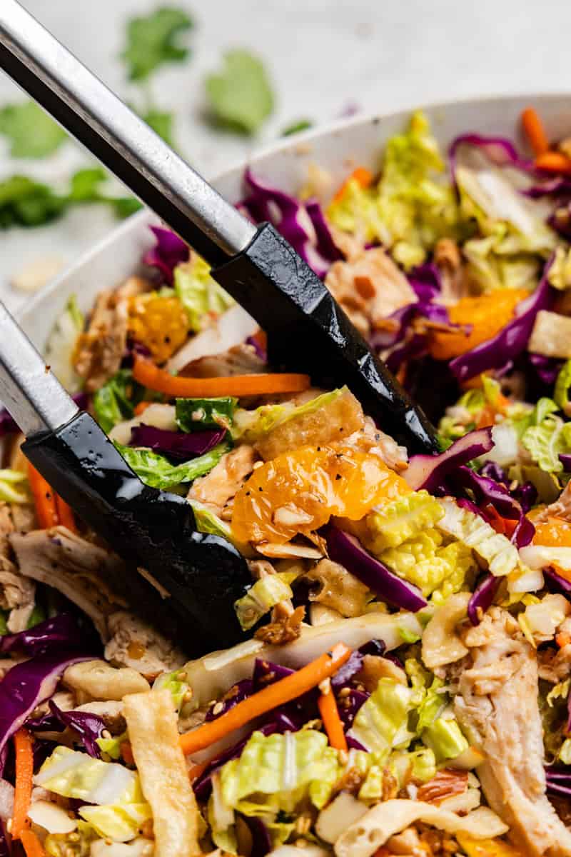 Closeup of Chinese chicken salad getting picked up by tongs.