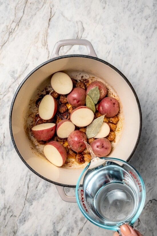 With spicy chorizo, potatoes, corn, crab, clams and shrimp, this seafood boil recipe is a complete meal in one pot. So easy to make too! Pouring water into Dutch oven with bay leaves and potatoes