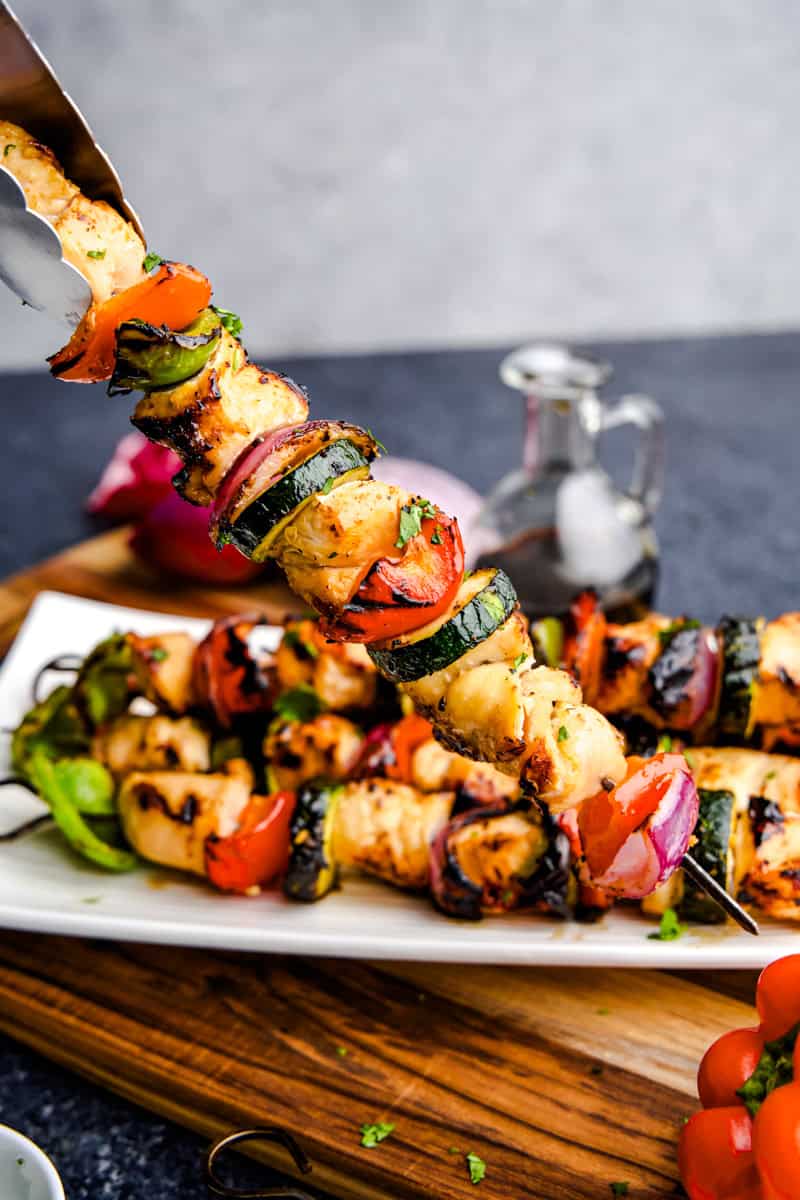 Tongs placing a juicy marinated grilled chicken kabob on a white plate.