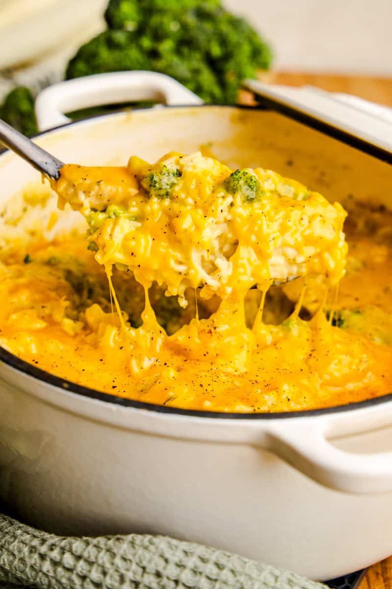 A Rolle Full Of Cheesy One Pot Chicken Broccoli & Rice in A White Cast Iron Pot.