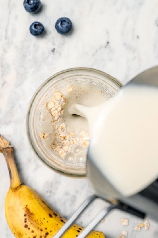 Overnight oats are the easiest way to work a healthy breakfast into your morning! No cooking required, they're a hearty breakfast packed with fiber, vitamins, and nutrients. Overhead view of milk being poured into jar of overnight oats
