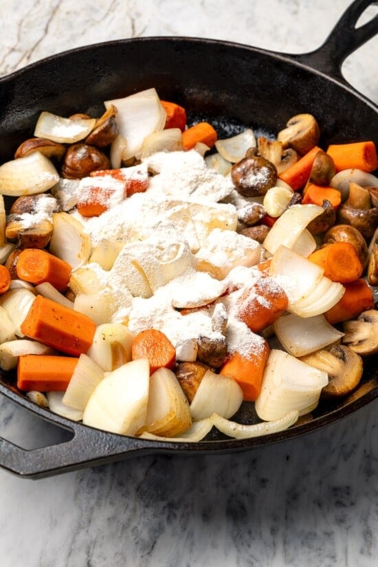 Flour sprinkled over vegetables in skillet.