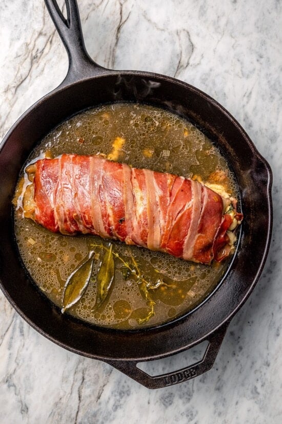 Skillet with prosciutto-wrapped stuffed turkey tenderloin and broth.