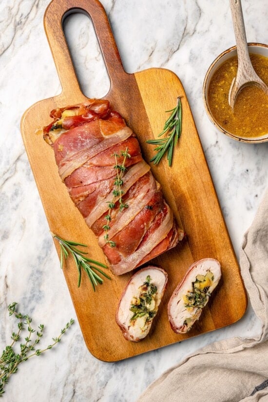 Two slices of prosciutto-wrapped stuffed turkey tenderloin next to remaining tenderloin.