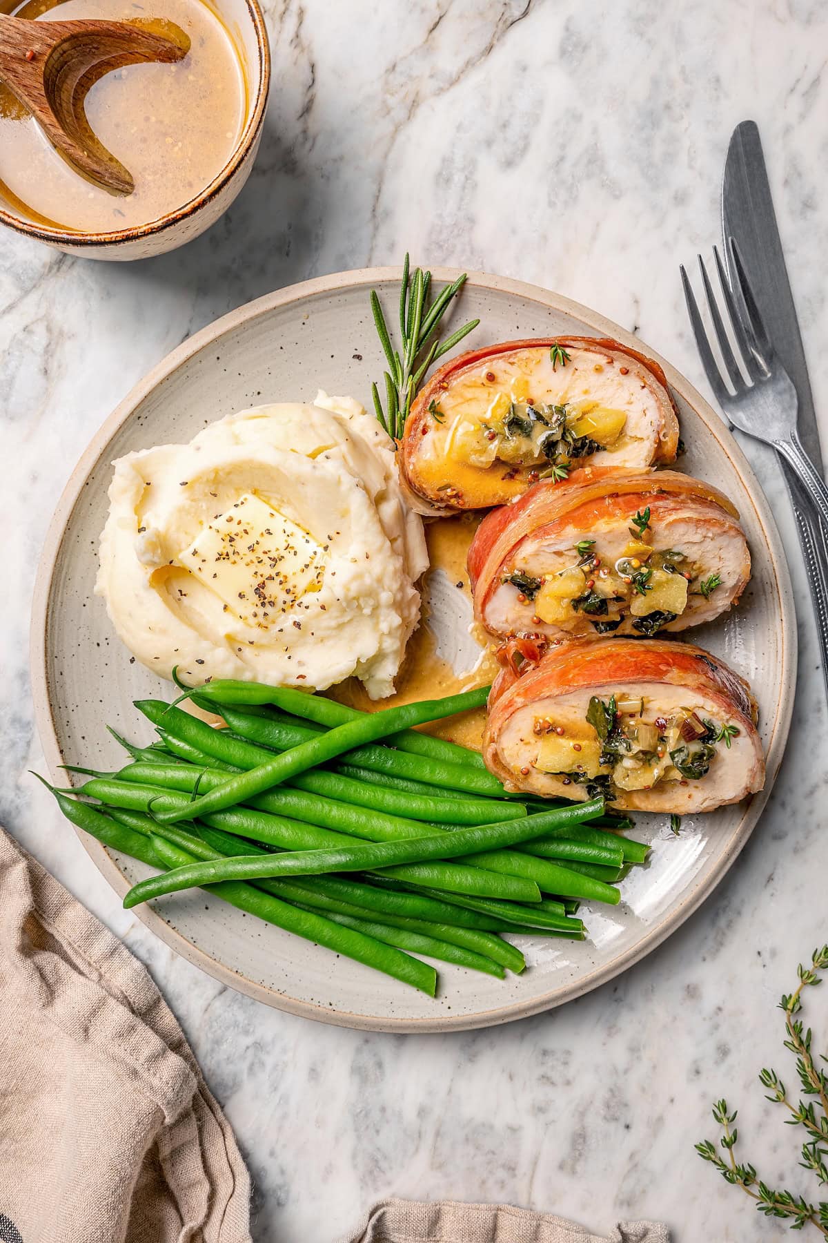 Plate of prosciutto-wrapped stuffed turkey tenderloin, green beans, and mashed potatoes.