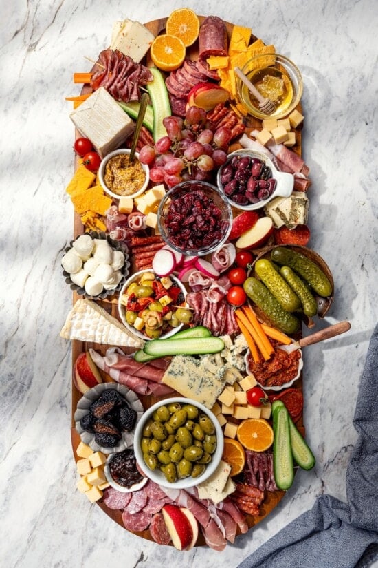 Charcuterie board in process, with cheese, meats, pickles, and more.