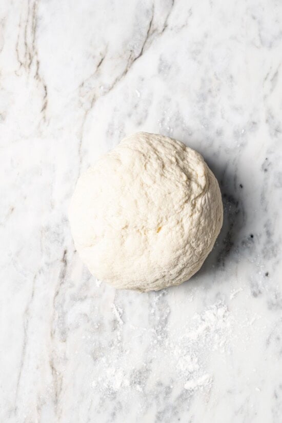 Breakfast pizza dough in ball on floured marble slab.