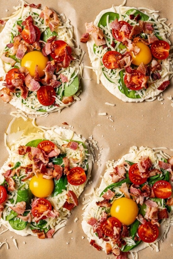 Unbaked breakfast pizzas on parchment paper.