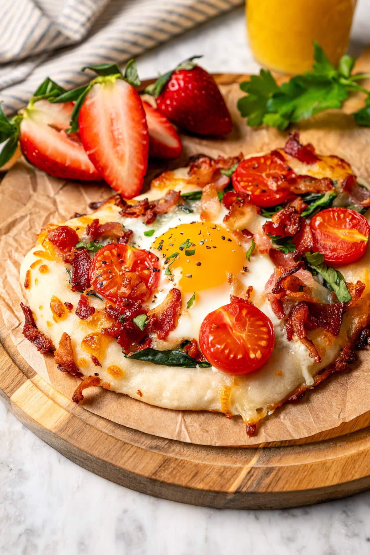 Breakfast pizza topped with egg, tomatoes, spinach, and bacon.