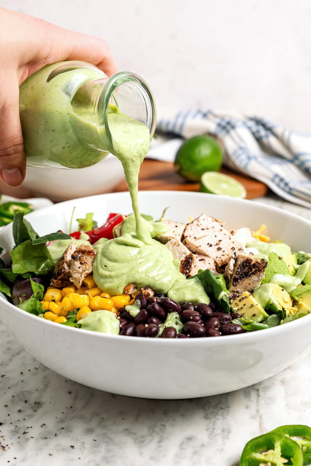 Pouring avocado cilantro lime dressing over salad in bowl.