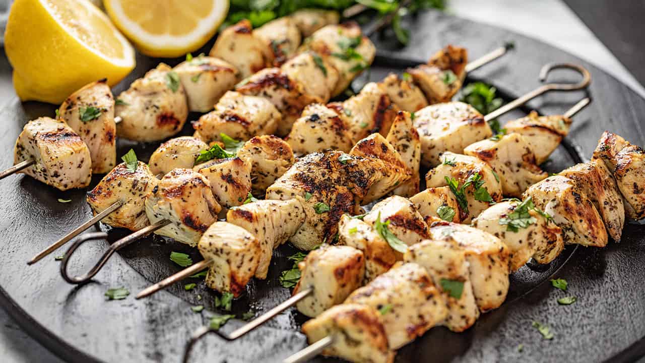 Lemon Chicken Kabobs garnished with lemon halves and parsley on a black plate.