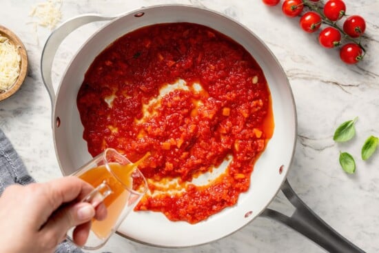 This healthy quinoa risotto swaps out the usual rice for protein-packed cooked quinoa. It's easy, creamy, and ready in just 15 minutes! Pouring broth into skillet of sauce.