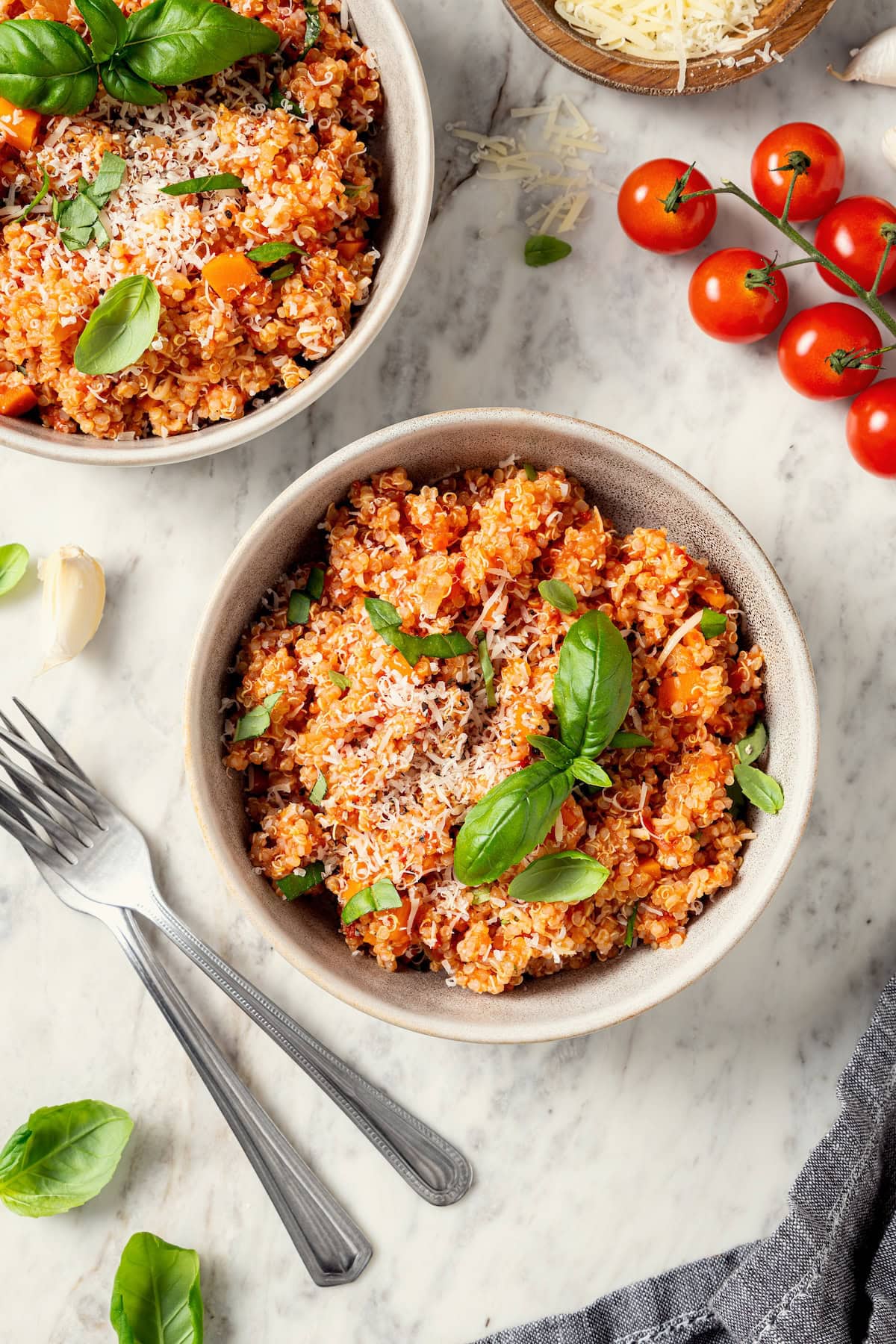 This healthy quinoa risotto swaps out the usual rice for protein-packed cooked quinoa. It's easy, creamy, and ready in just 15 minutes! Two bowls of quinoa risotto with cheese and fresh basil.