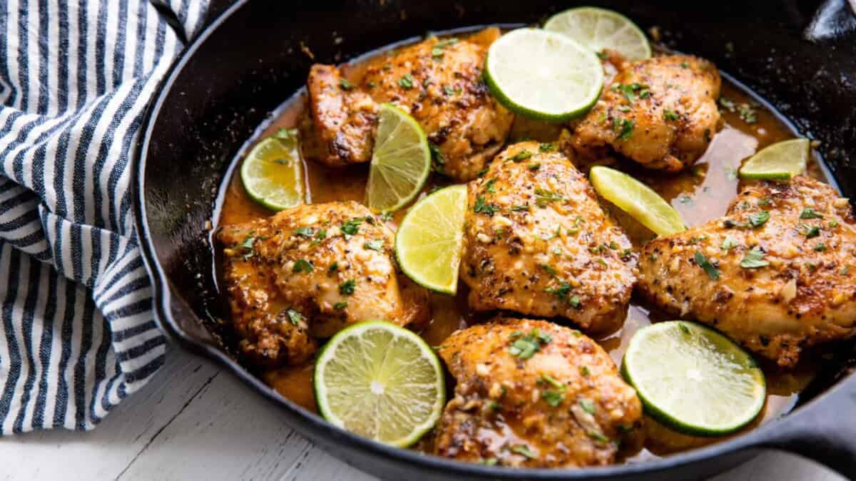 A skillet of garlic lime chicken topped with lime slices.