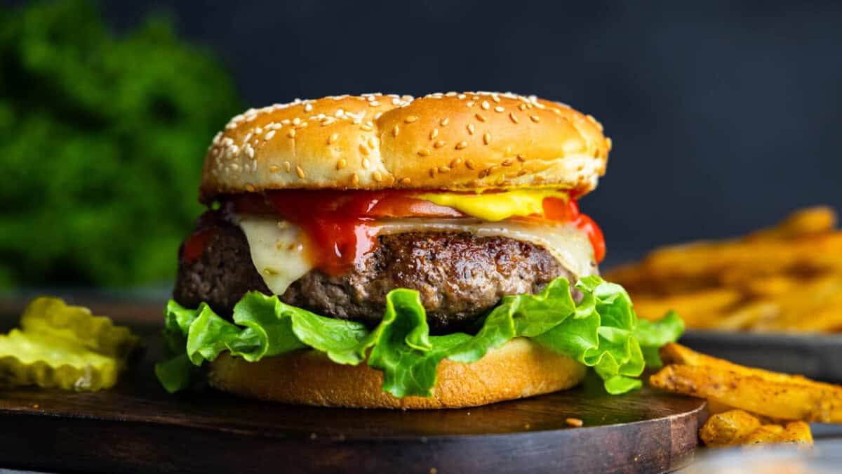 A close up view of a perfect juicy hamburger on a black plate with french fries in the background.