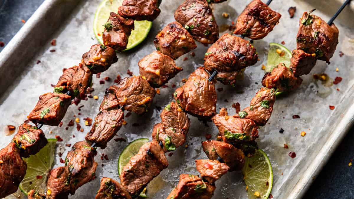 Four marinated beef kebabs are laid out on a tray.