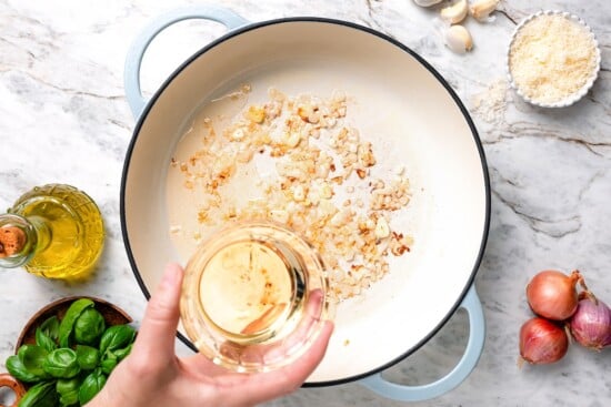 With tender mussels in cream sauce with Parmesan and basil, this recipe is perfect for special occasions, but easy enough for a weeknight! Hand holding wine above skillet with aromatics.
