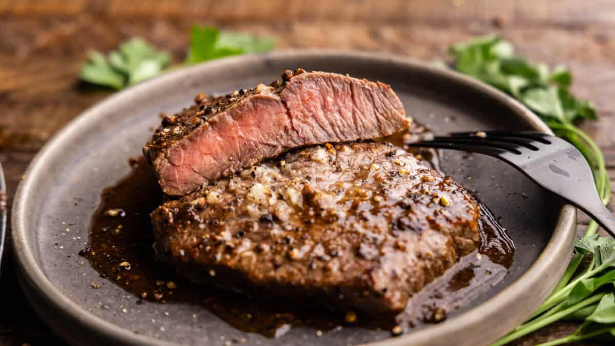 A close up view of a sirloin steak on a gray plate that has been cut in half to show the pink interior.