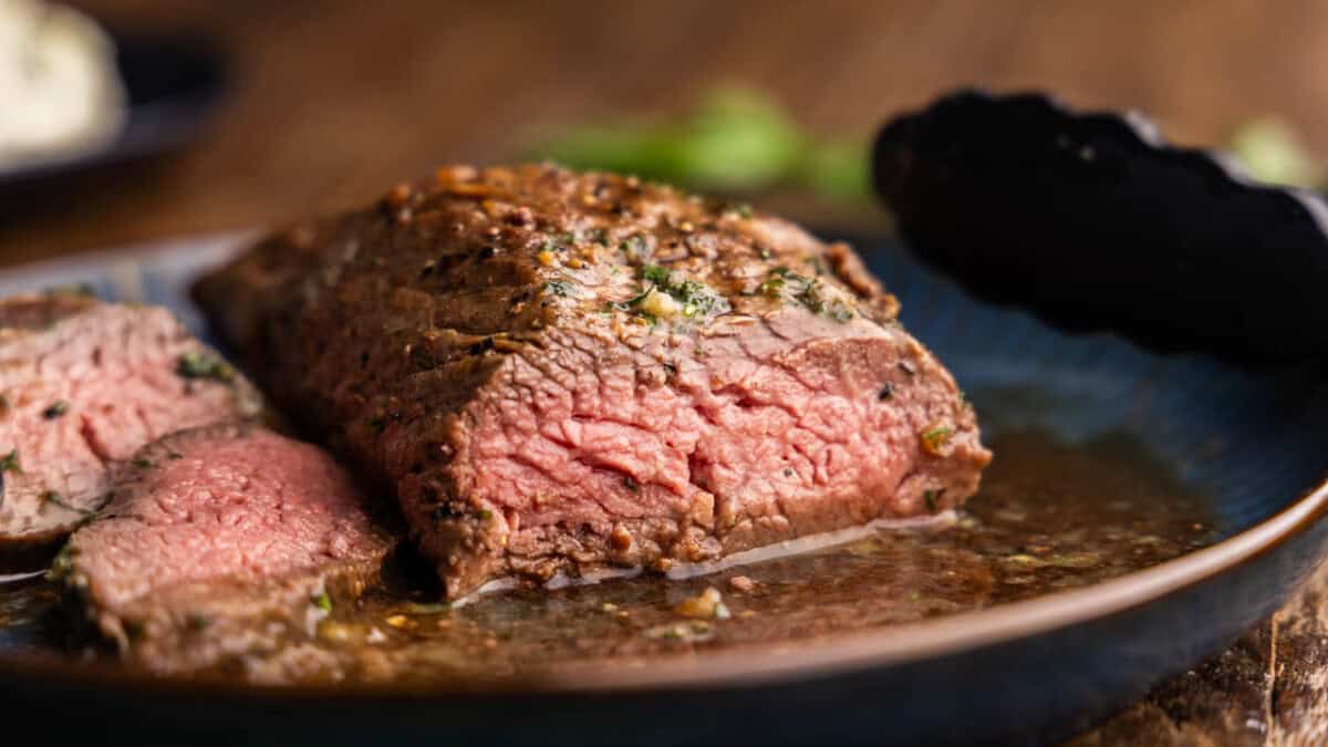 A close up view of a petite tender steak that has already been cut into showing a perfectly pink interior.