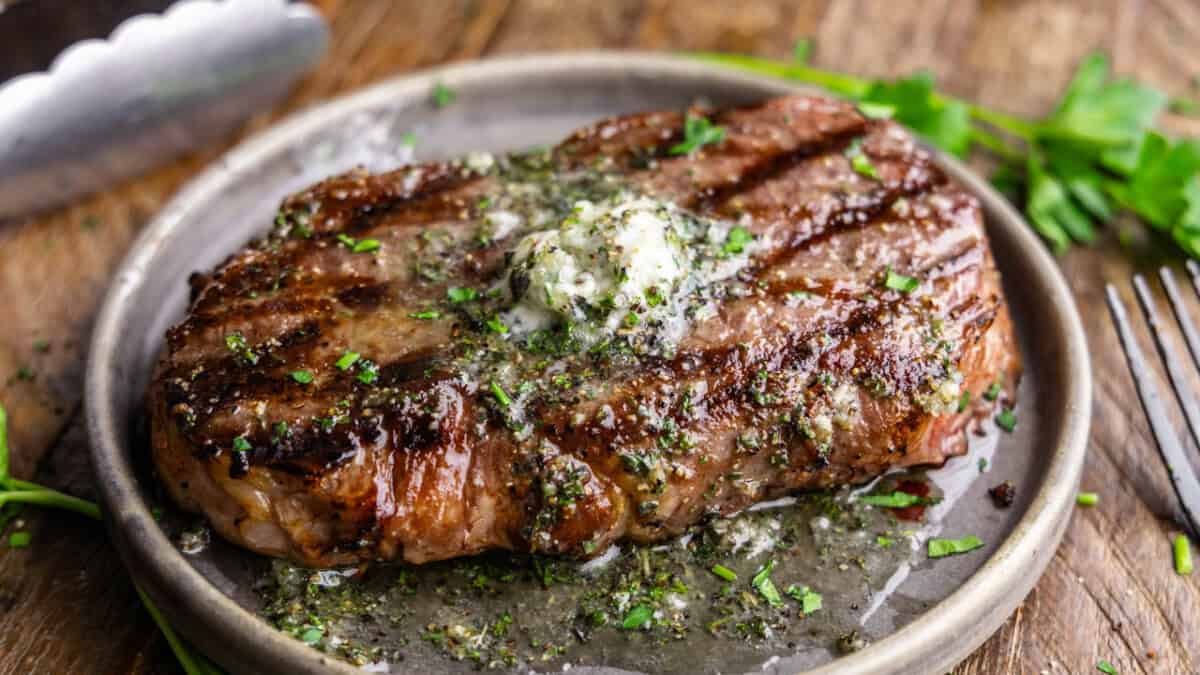 A perfectly grilled steak on a gray plate with resting butter melting on top.