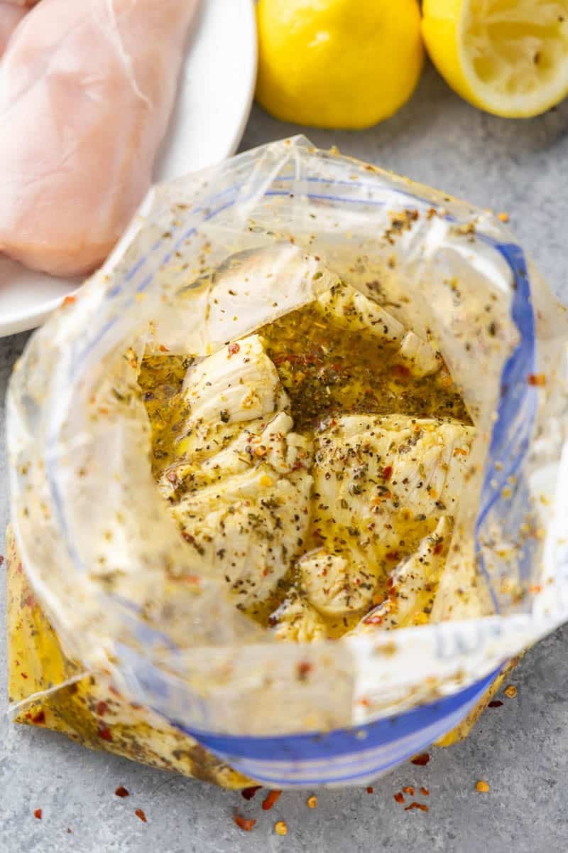 Close-up of juicy raw chicken breasts submerged in homemade lemon pepper chicken marinade with garlic, herbs, lemon juice, and olive oil.