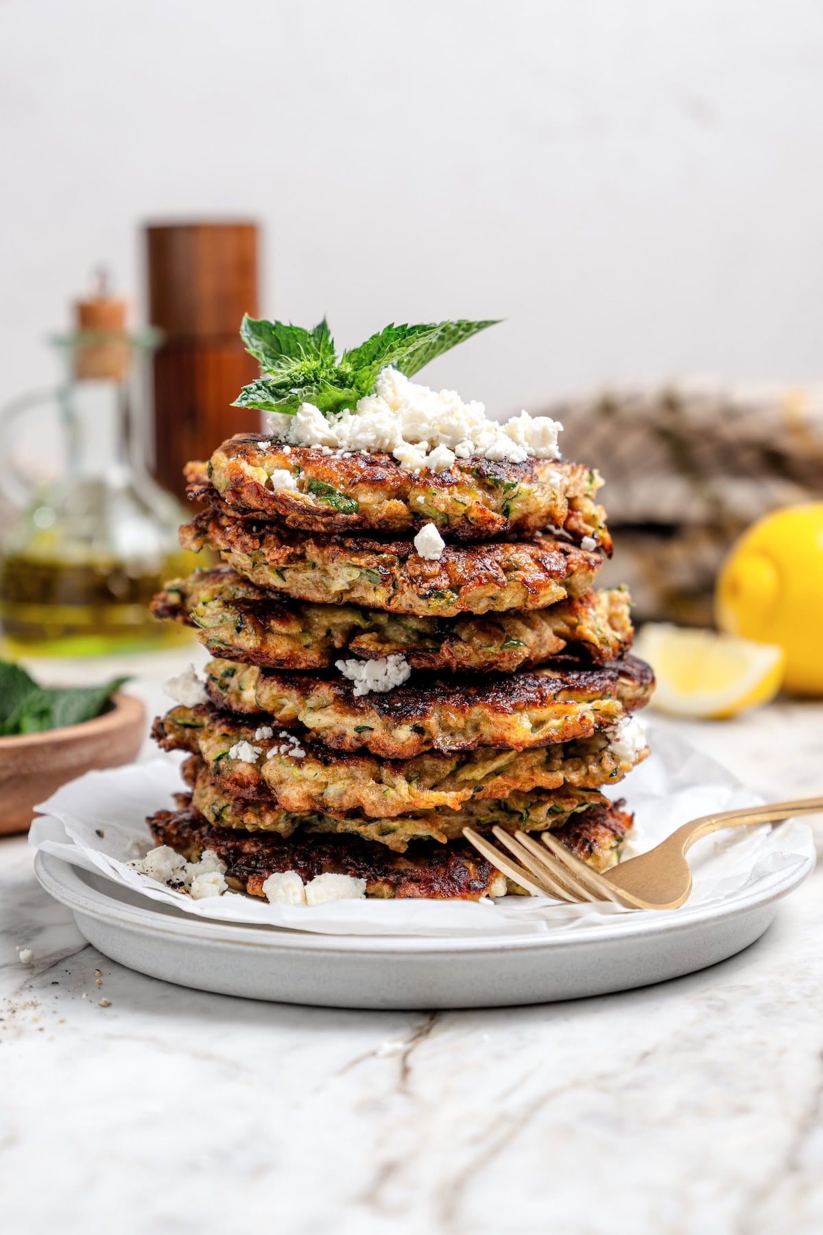 Stack of zucchini fritters on plate with feta and mint.
