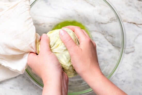 Hands squeezing zucchini wrapped in cheesecloth to remove moisture.