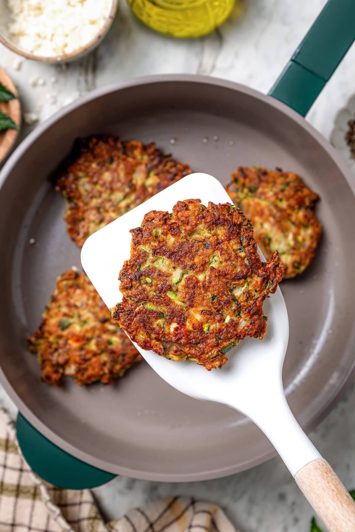 Spatula holding zucchini fritter over skillet.