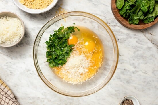 This cozy stracciatella soup is made with rich chicken broth, Parmesan, orzo and spinach for a satisfying meal. Done in just 20 minutes! Eggs, Parmesan, and parsley in glass bowl.