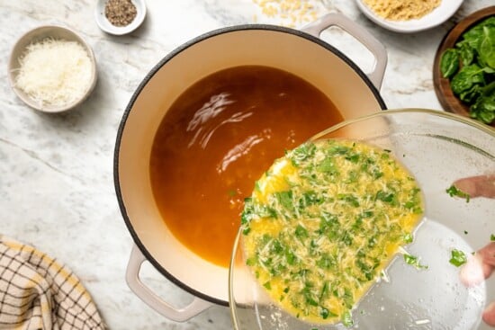 This cozy stracciatella soup is made with rich chicken broth, Parmesan, orzo and spinach for a satisfying meal. Done in just 20 minutes! Pouring egg mixture into pot of broth.