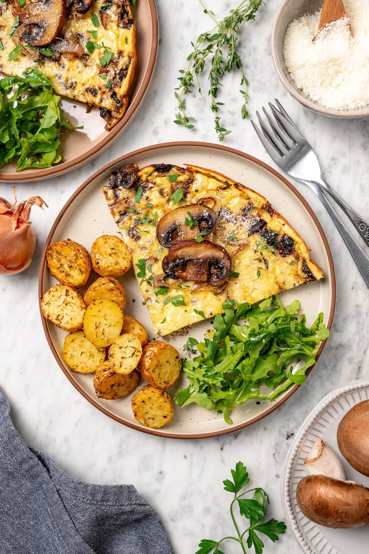 This aromatic mushroom frittata with egg whites, sautéed mushrooms, shallots, and cheese is an easy-to-make gourmet breakfast or brunch. Overhead view of a slice of mushroom frittata served with crispy potatoes and fresh greens on a plate.