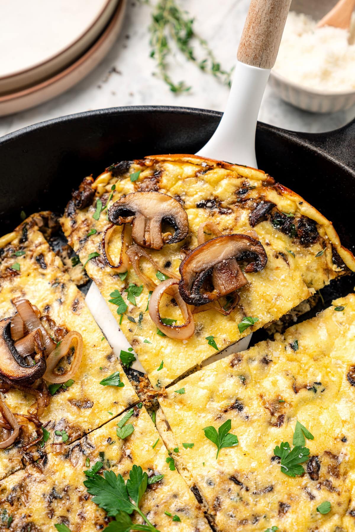 This aromatic mushroom frittata with egg whites, sautéed mushrooms, shallots, and cheese is an easy-to-make gourmet breakfast or brunch. A spatula lifting a slice of mushroom frittata from a cast-iron skillet.