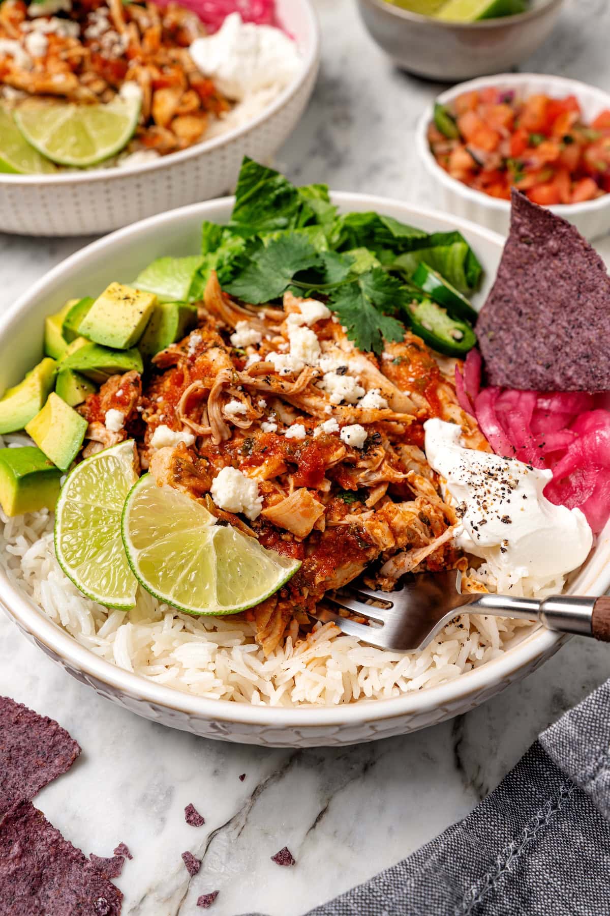 The easiest crockpot salsa chicken with juicy chicken thighs, jarred salsa, and simple spices. Great for meal prep, tacos, and rice bowls! A crockpot salsa chicken bowl served over a bed of rice, garnished with avocado, pickled onions, jalapeño, and more toppings.