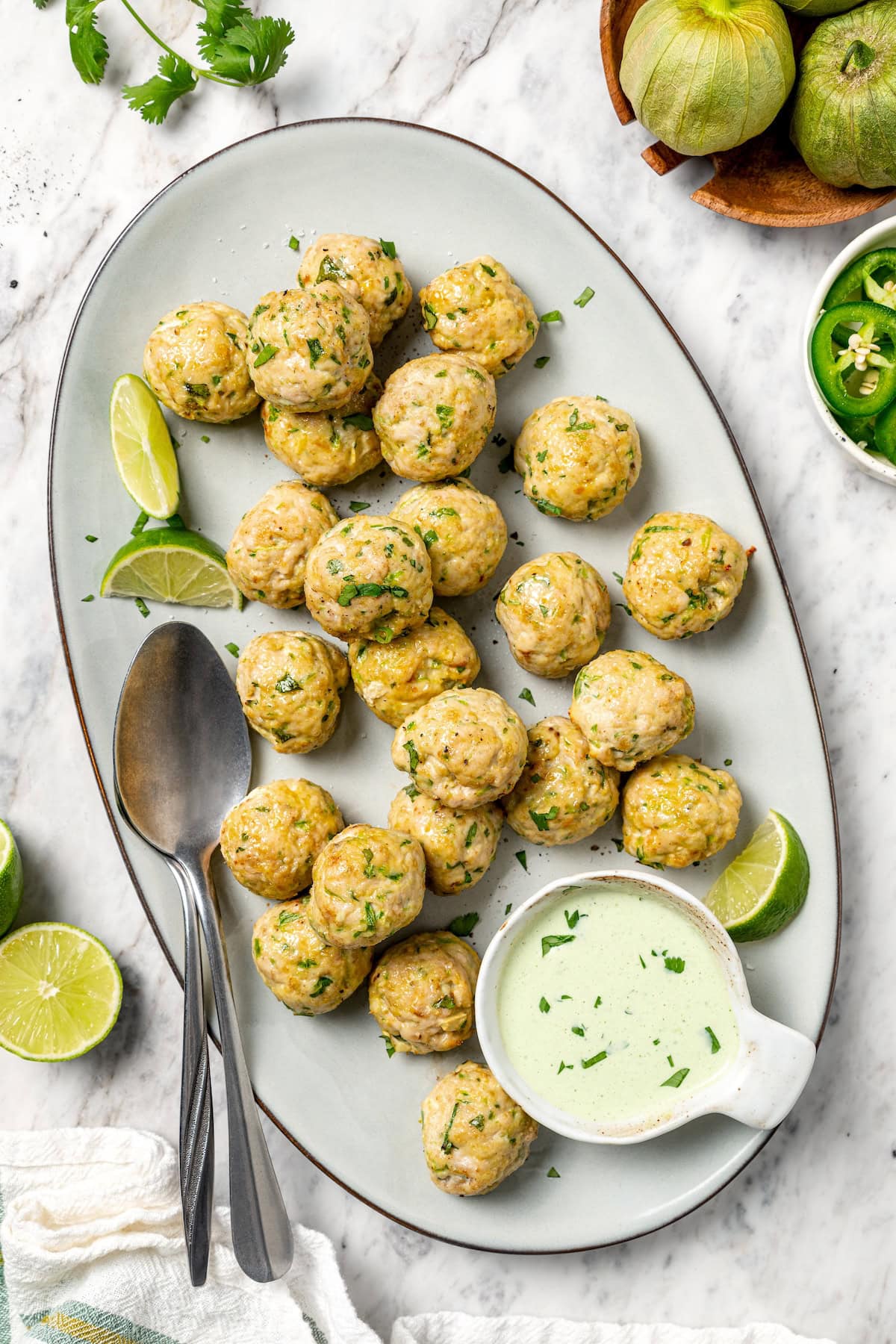 These Southwest baked turkey meatballs are made with jalapeño, cilantro and cumin for a light, tasty twist on classic meatballs! Add them to meal bowls and salads or serve them as an appetizer. Baked southwest turkey meatballs on platter with bowl of creamy cilantro sauce.