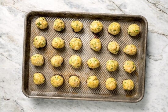 These Southwest baked turkey meatballs are made with jalapeño, cilantro and cumin for a light, tasty twist on classic meatballs! Add them to meal bowls and salads or serve them as an appetizer. Rimmed baking sheet with baked southwest turkey meatballs.